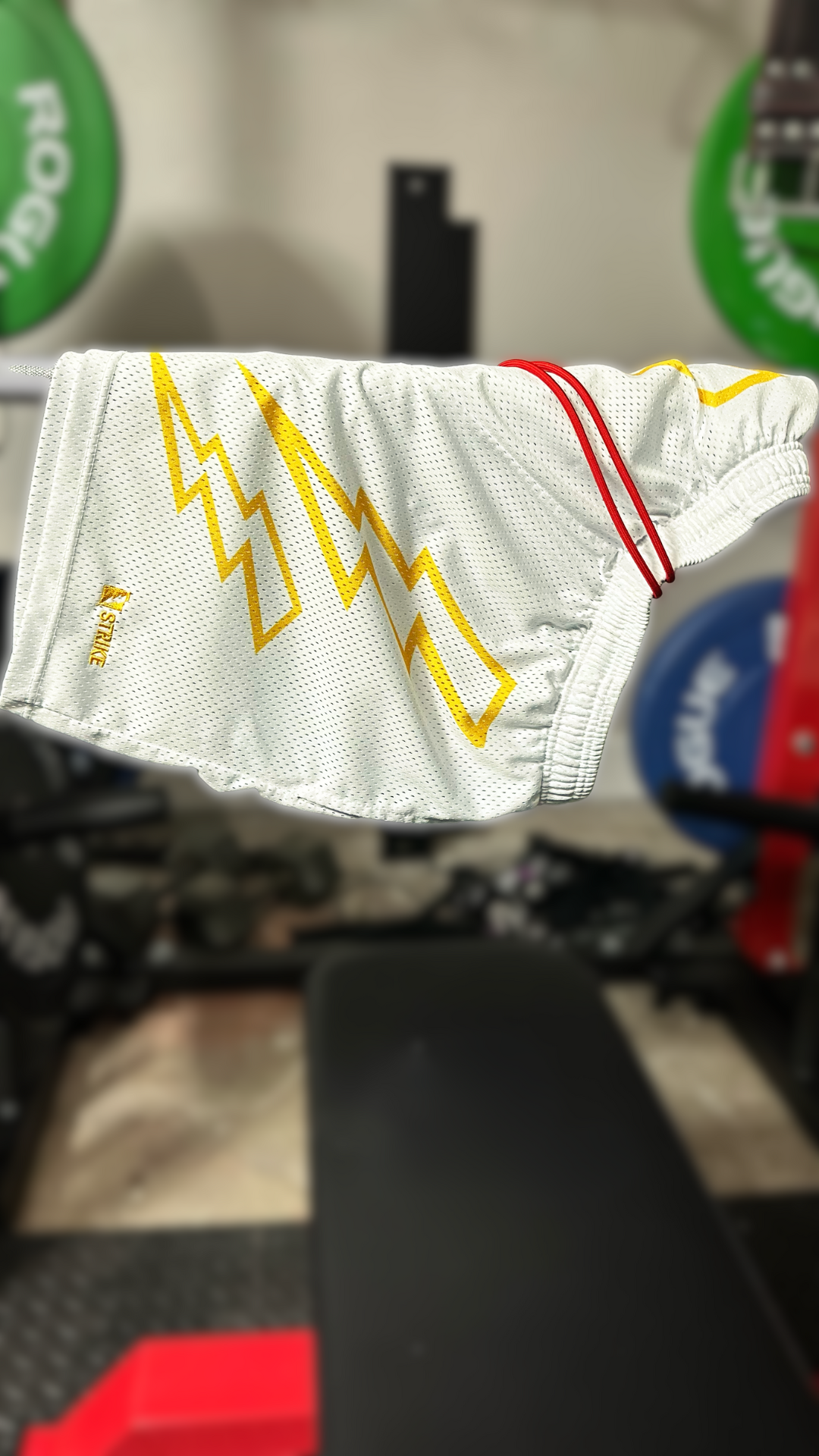 White shorts with two yellow three tired lightening bolts on both thighs hung on the barbell above the bench.